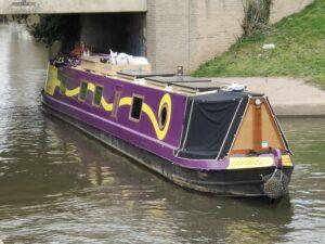 Narrowboat Sola Gratia, purple with a yellow swirl, cruising on the River Soar in March 2022.